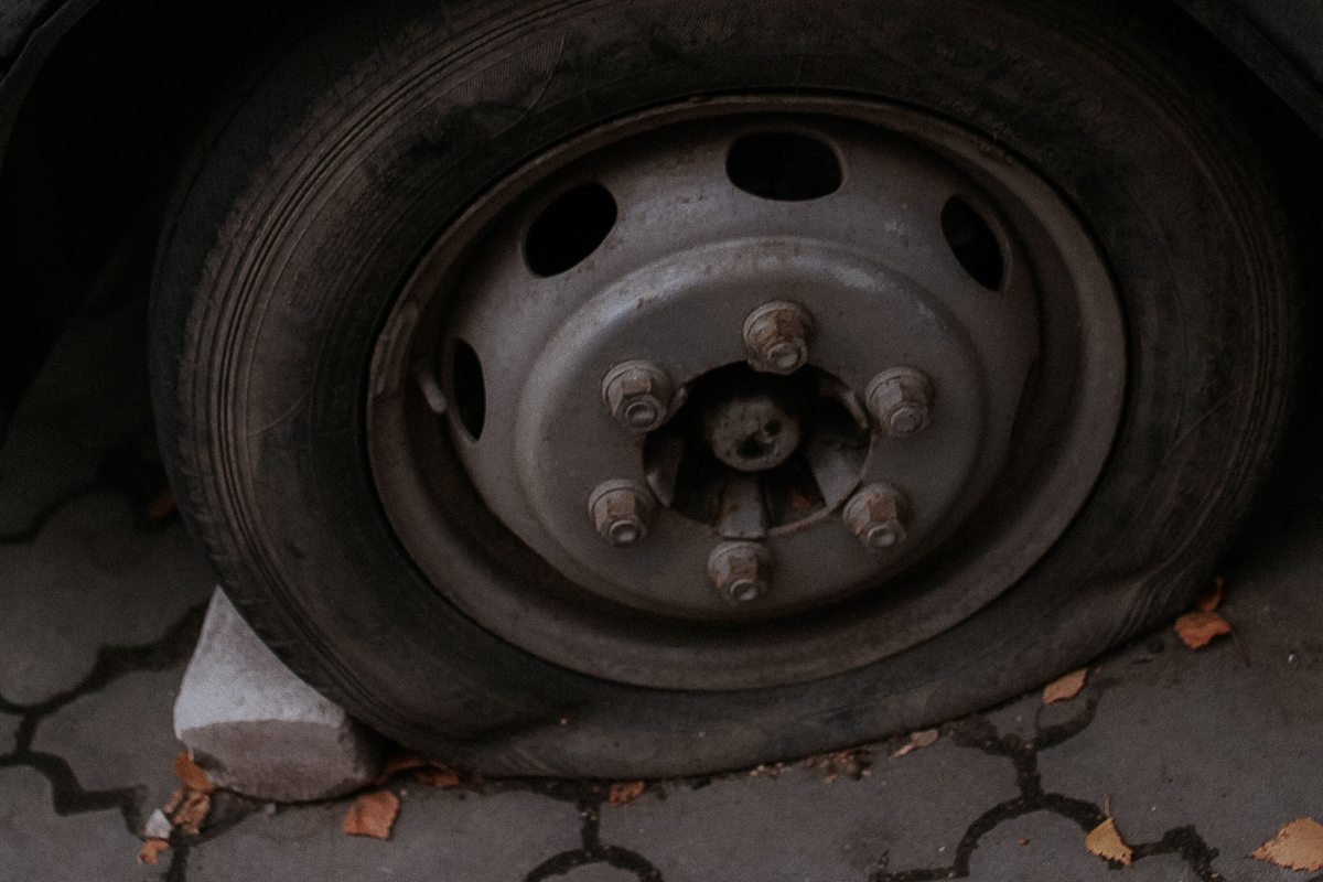 Deflated tire on a dark car beside a paved surface.