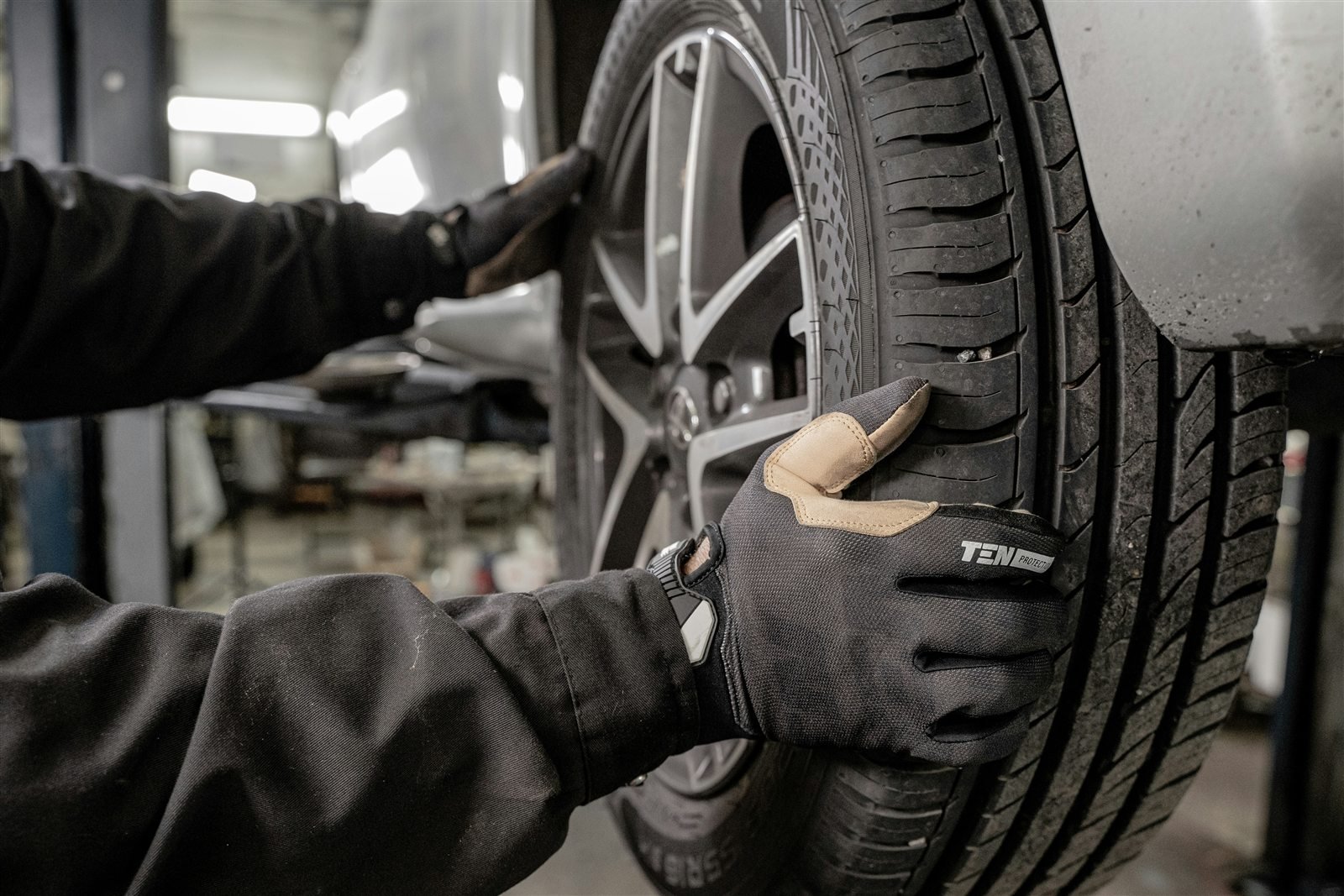 Gloved hands positioning a wheel on a vehicle in a workshop.